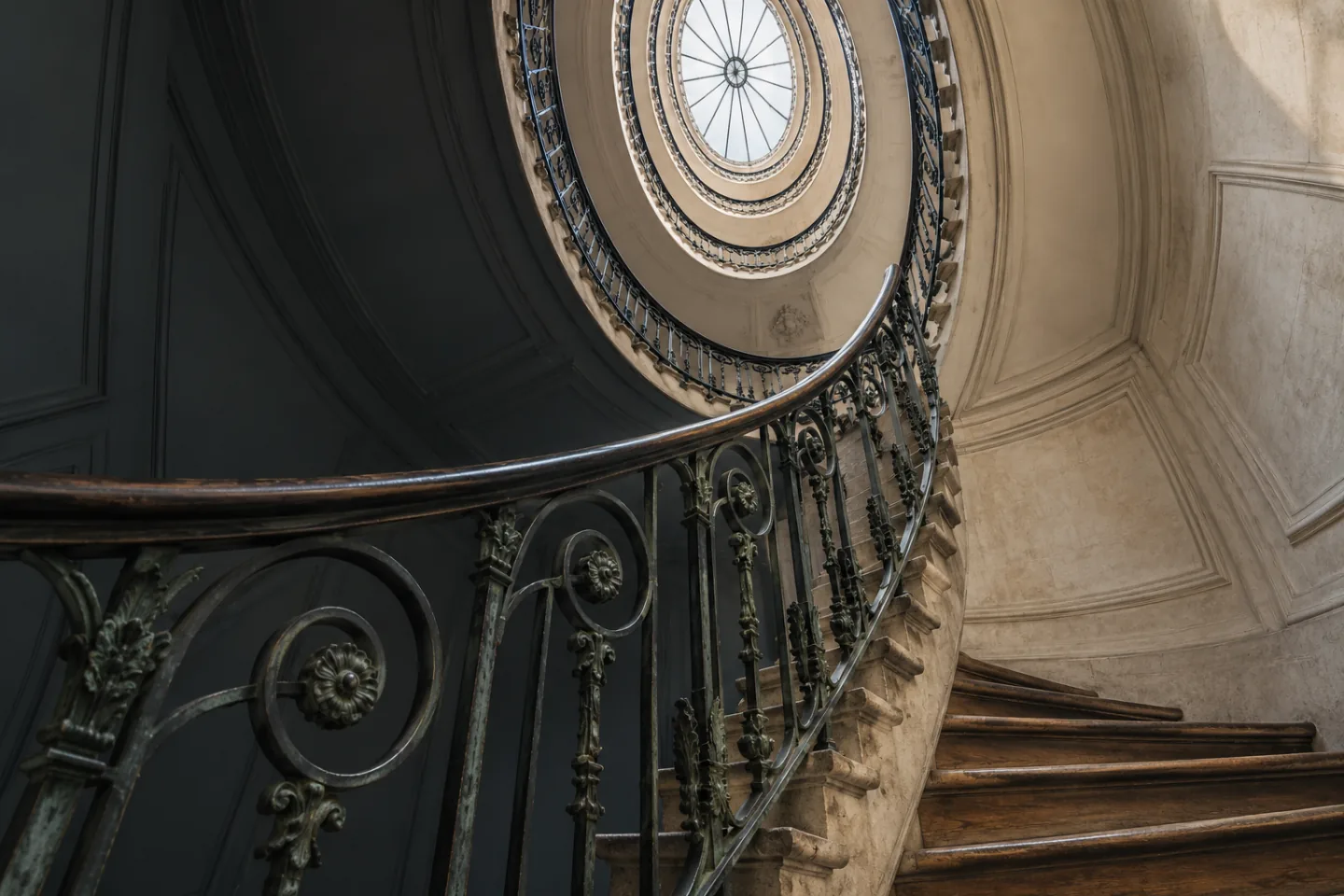 Cage d’escalier ovale d’un immeuble ancien vue d’en bas, rampe en fer forgé et verrière zénithale